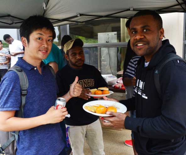 three men hold plates of food at an outdoor pavilion